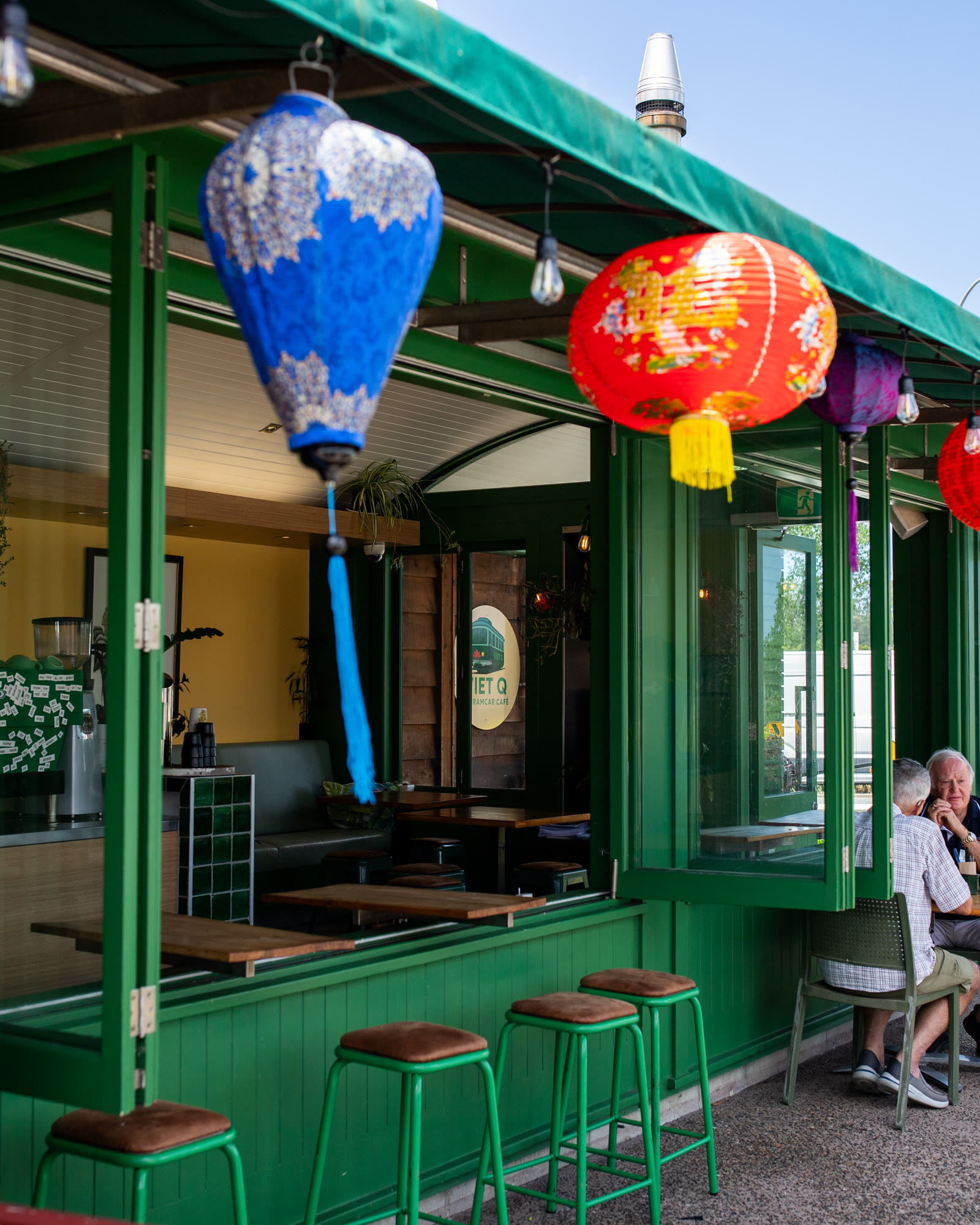 Viet Q at Tramcar, Matakana Village: the green tramcar with its bifold windows open, paper lanterns strung along the awning, stools at the counter, and two customers at a table outside.