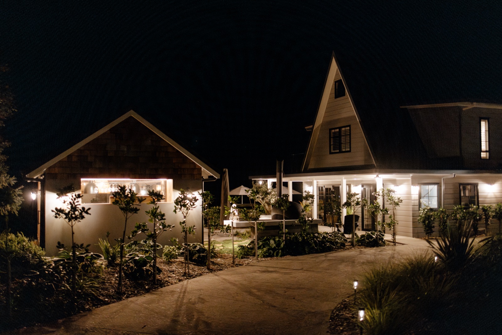 The Cookhouse and the Farmhouse at Bluestone Ridge lit at night after a wedding, the pizza oven glowing, path lights along the drive.